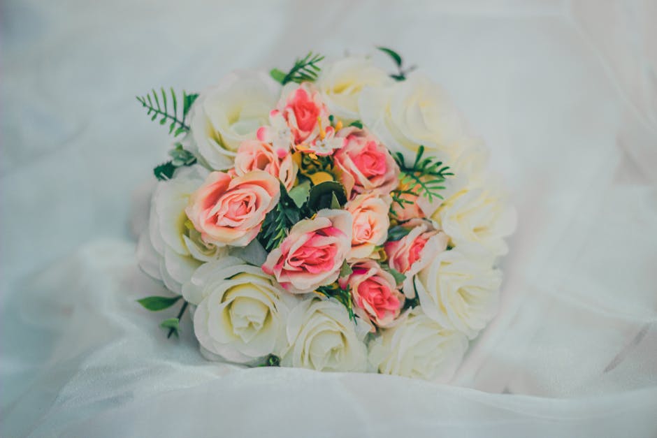 A floral arrangement featuring a bouquet of fresh cream-colored roses with soft, layered petals and vibrant pink roses with tightly curled petals at the center. The roses are accented with sprigs of g