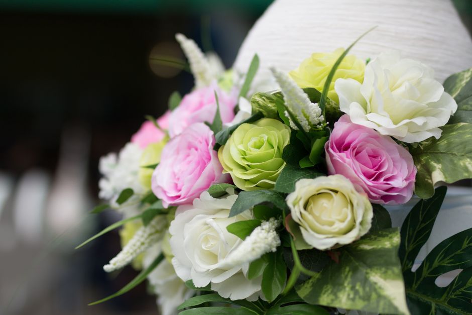 A close-up of a floral bouquet featuring a mix of fresh flowers including white and pale pink roses, light green roses, and white lisianthus, arranged with lush green foliage and accentuated with smal
